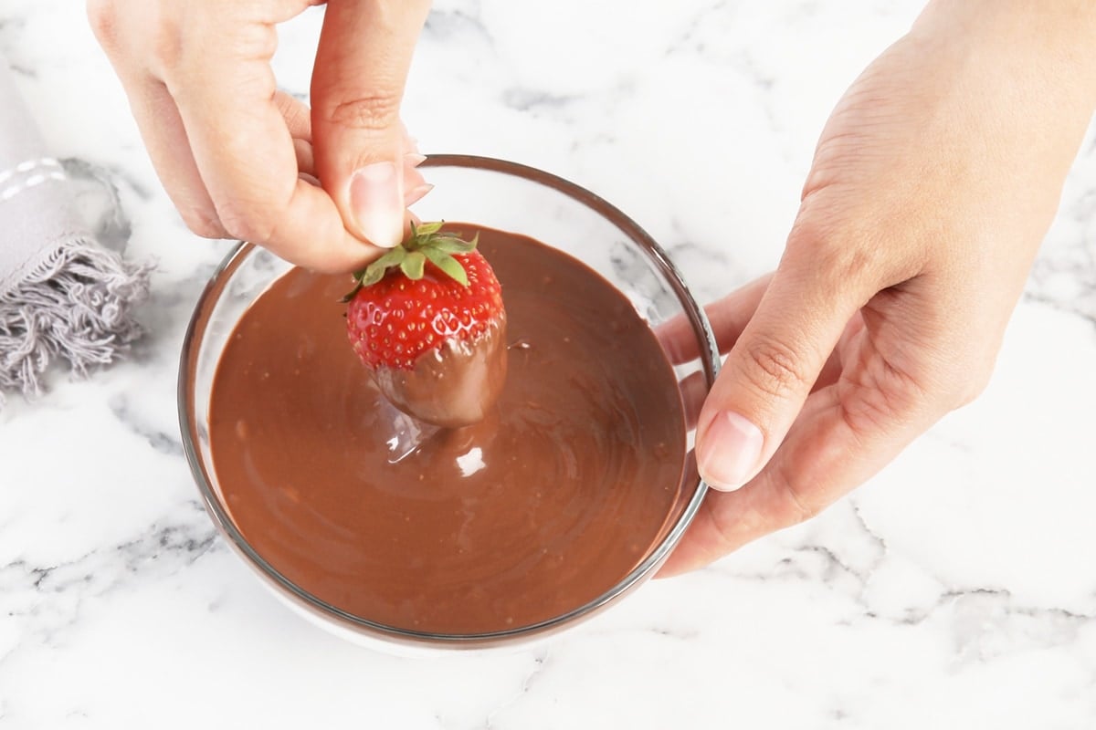 hand dipping strawberry in melted chocolate  