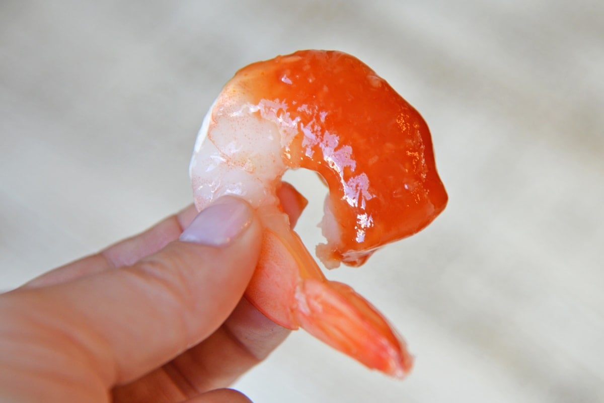 hand holding up a shrimp with cocktail sauce 