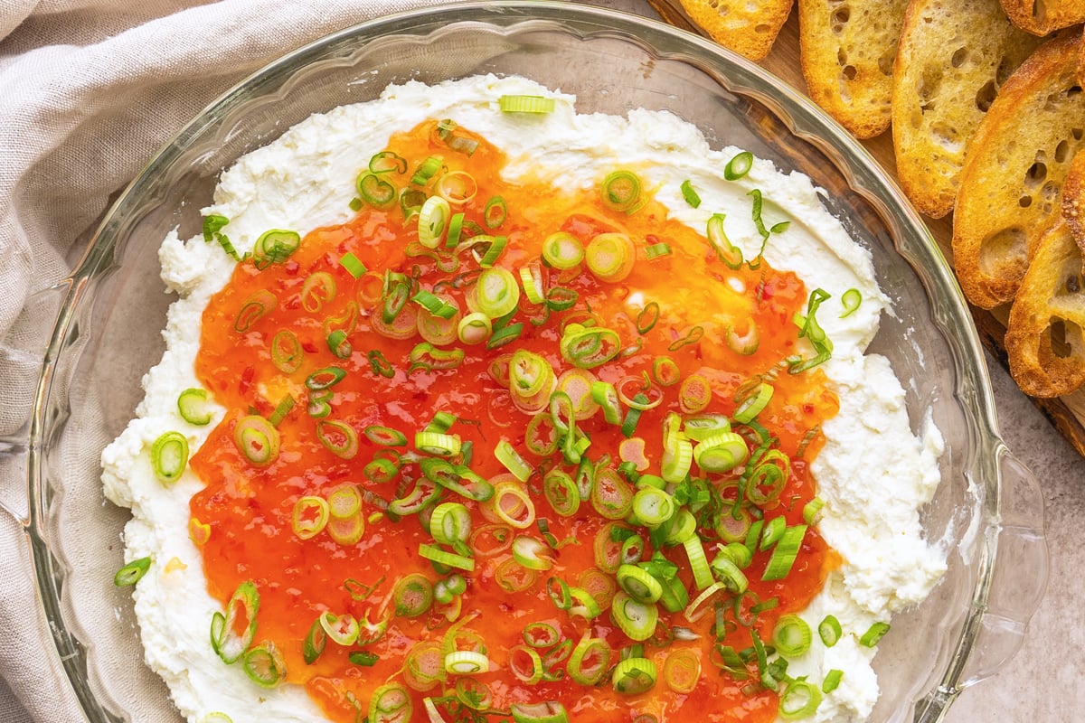 overhead of goat cheese dip topped with pepper jelly and scallions 