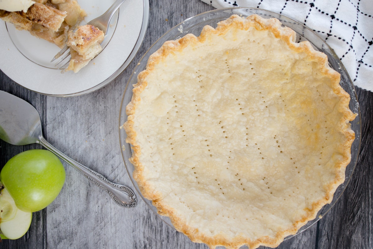 docked cooked pie crust with apple pie sitting near by