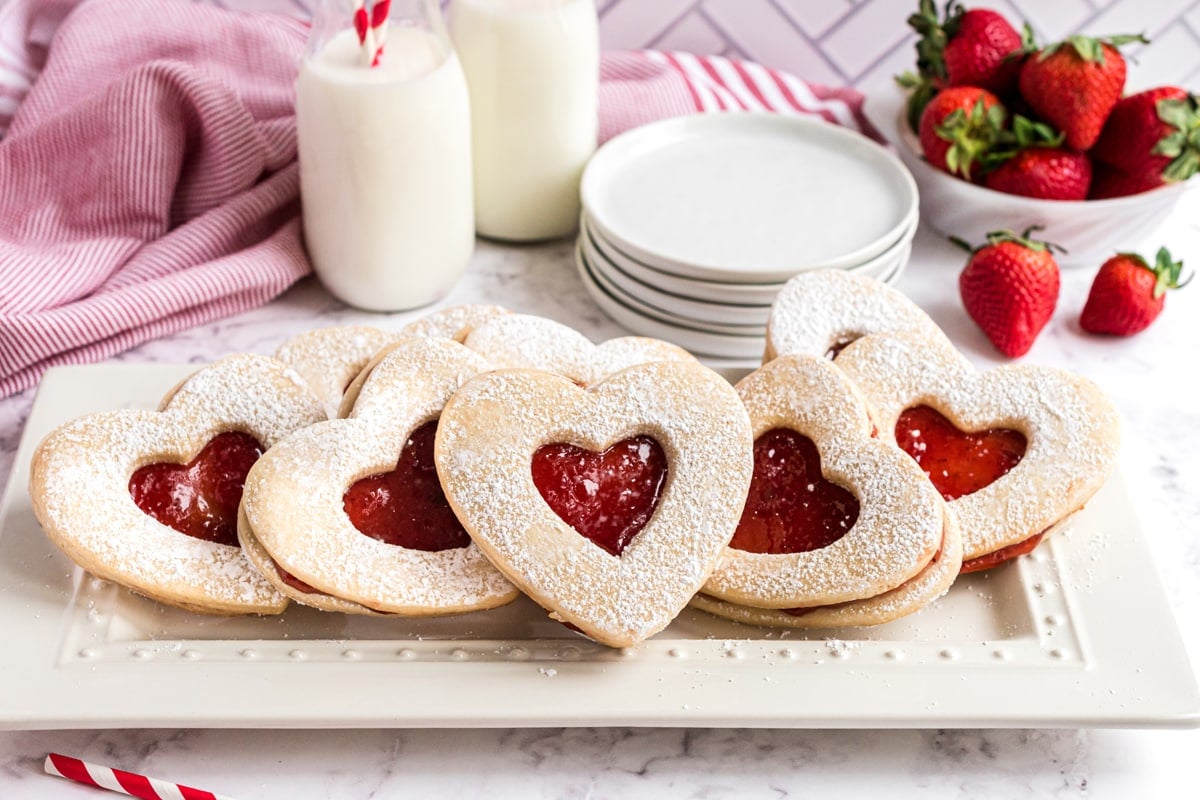 white serving platter of strawberry jam cookies with milk and small white plates