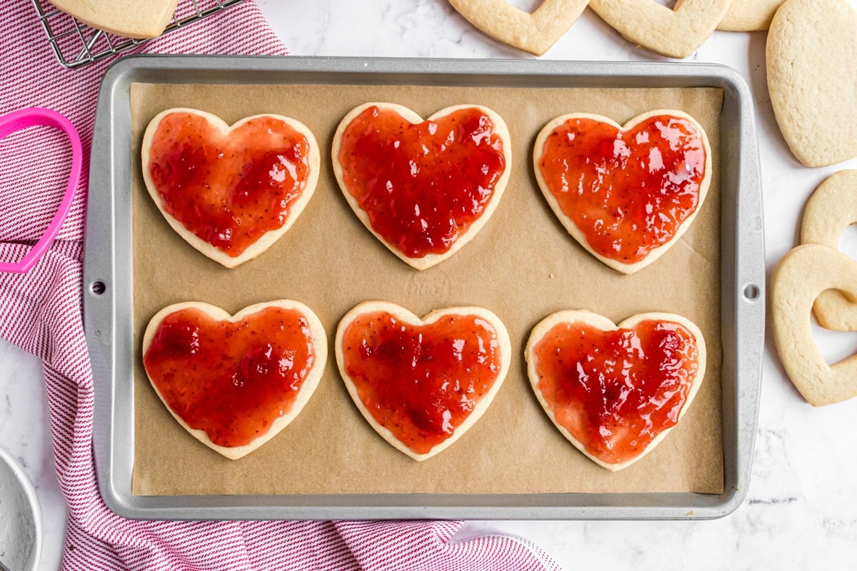 strawberry jam on sugar cookies on a baking sheet 