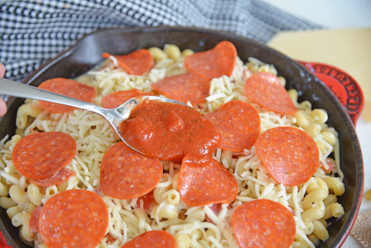 spooning tomato sauce over pepperonis and pasta 