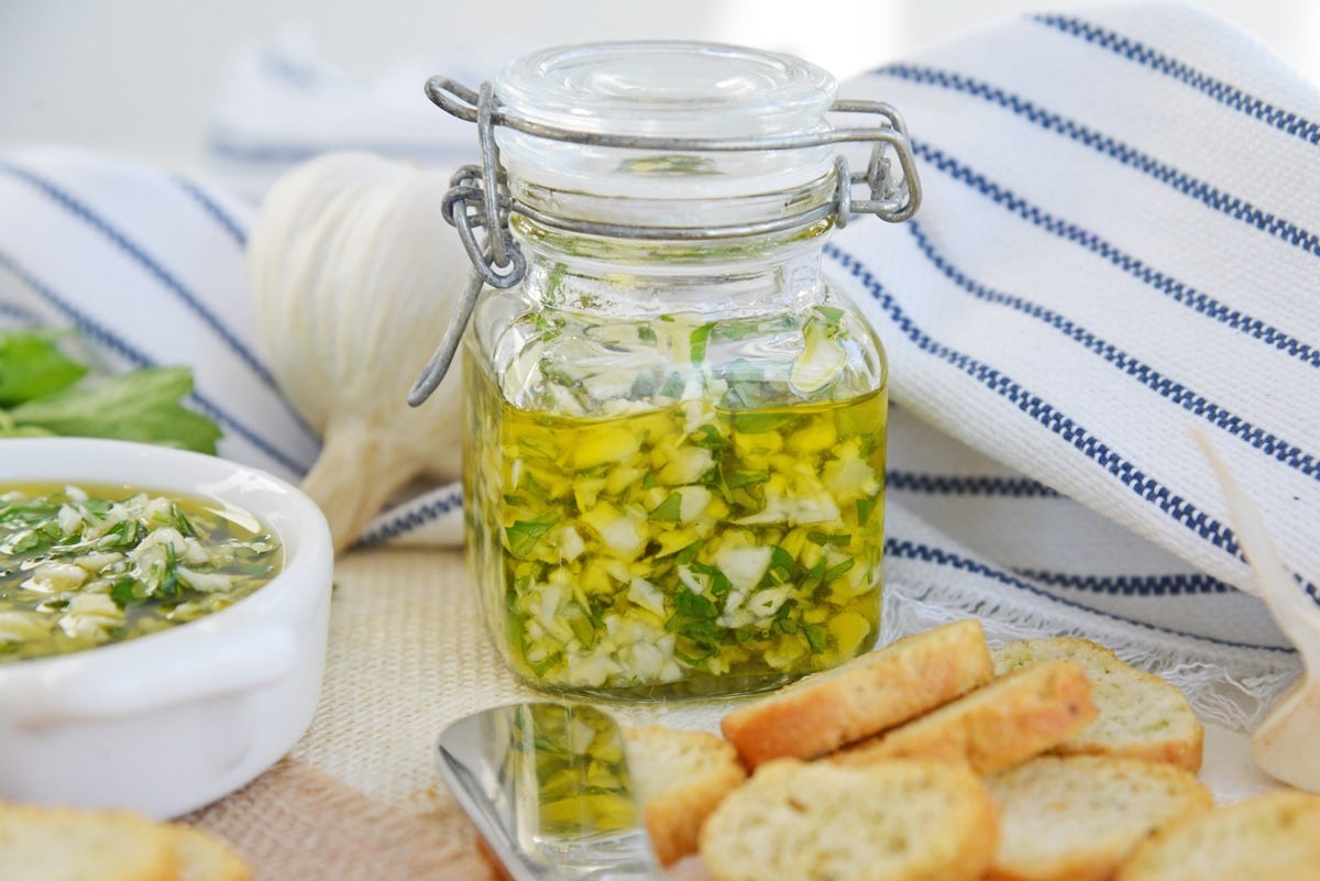 side view of garlic relish in a glass jar with crostini around 