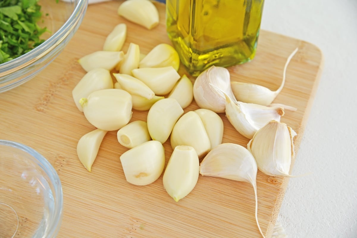 raw garlic cloves on a wood cutting board 