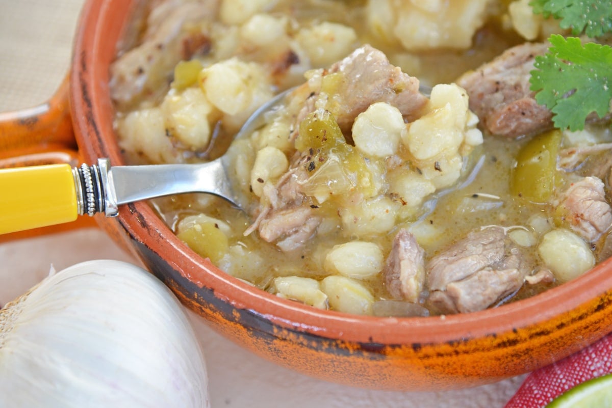 spoon digging into a bowl of pork pozole 