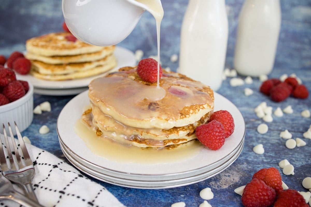 syrup pouring over a stack of raspberry pancakes