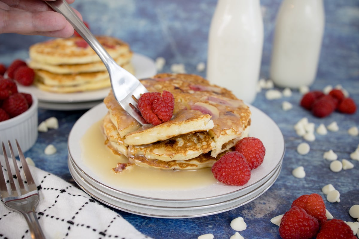 fork digging into raspberry pancakes with syrup 