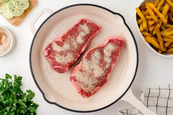 seasoned steaks in a white cast iron skillet