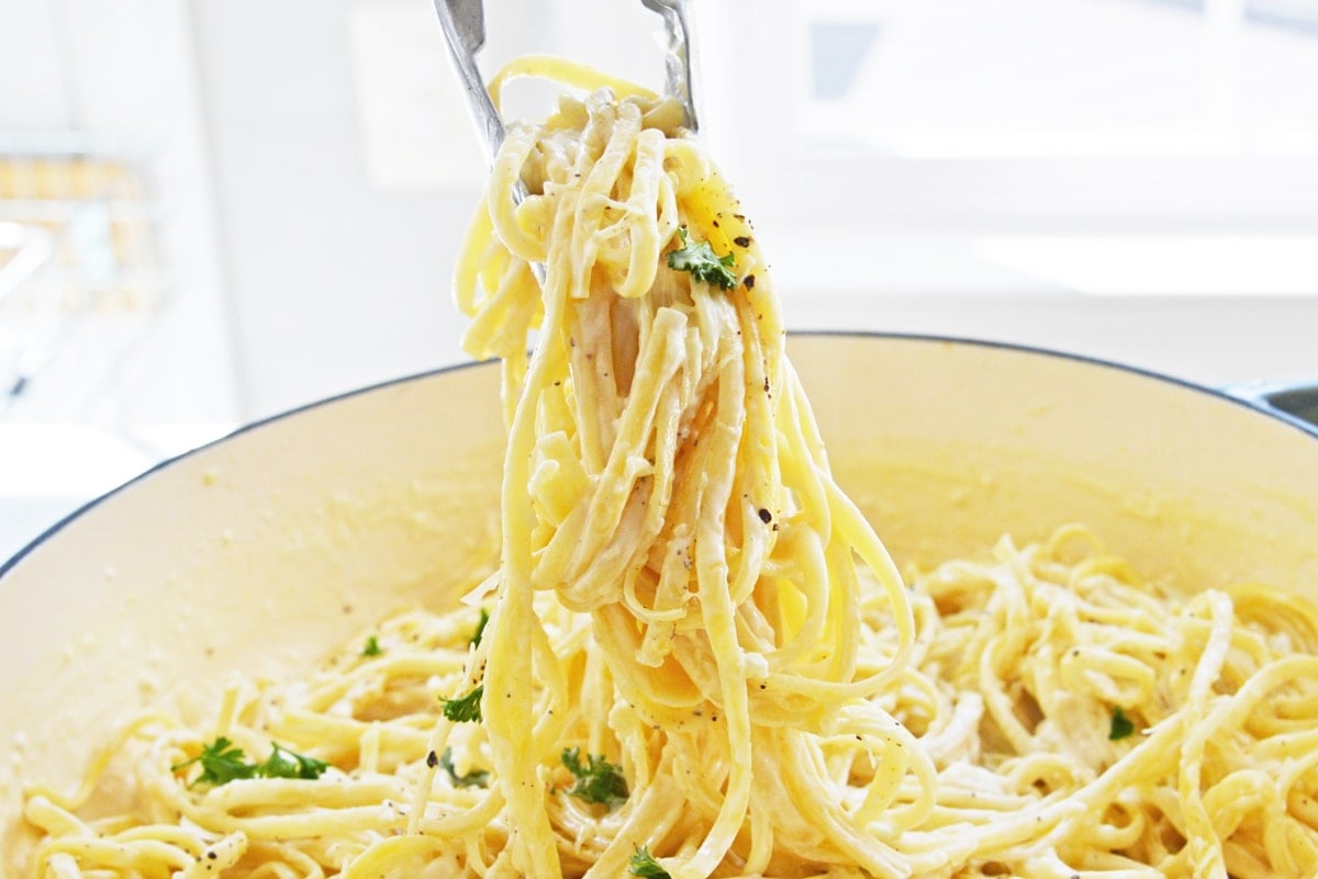 tongs tossing creamy linguine pasta 