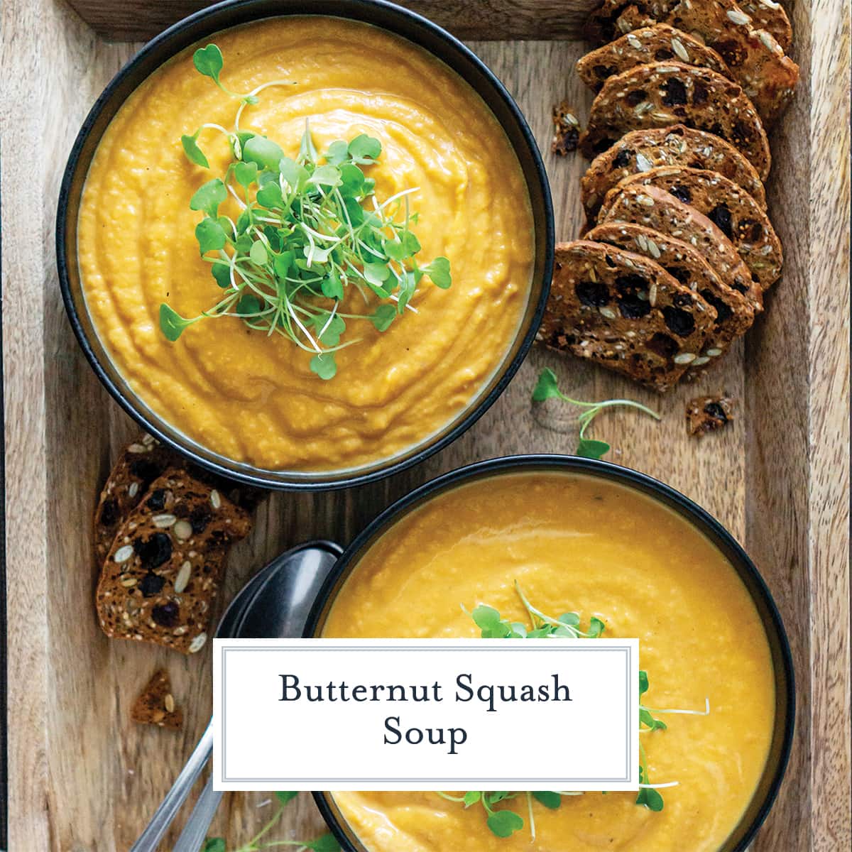 two bowls of creamy butternut squash soup on a serving board with toasts 