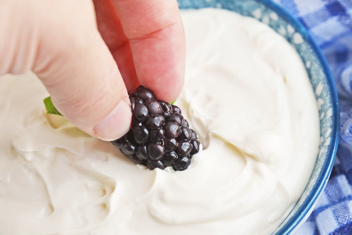 hand dipping blackberry in bowl of cream cheese fruit dip