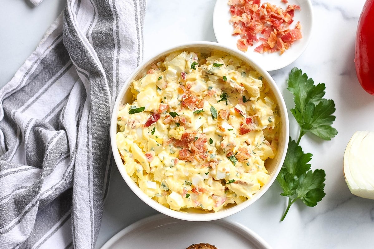 egg salad in a serving bowl with fresh ingredients around it  