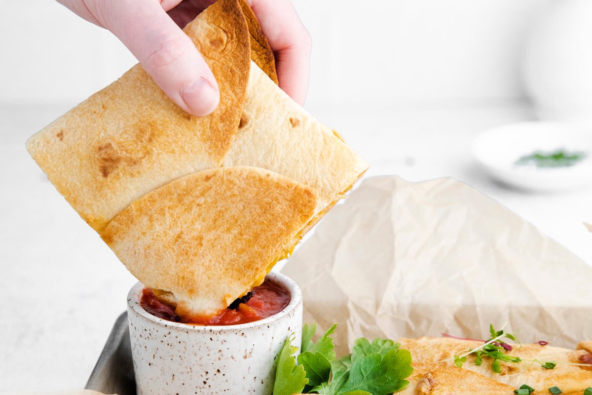 dipping a sheet pan quesadilla in the oven in homemade salsa 