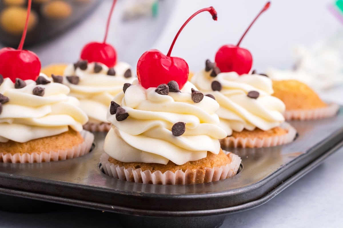 These EASY Cannoli Cupcakes are stuffed with classic cannoli filling, topped with cream cheese frosting and topped with cherries & chips. #cannolicupcakes #easycannolicupcakes www.savoryexperiments.com