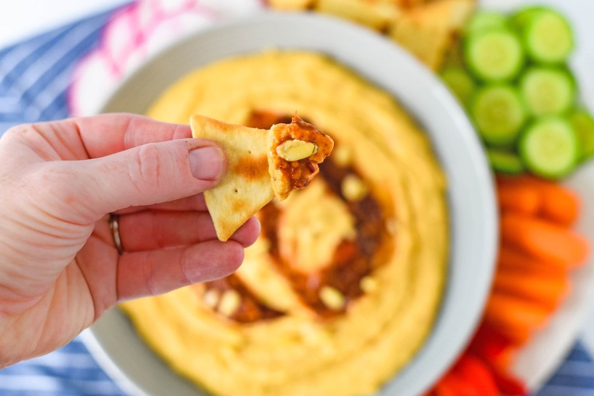 hand holding a pita chip with hummus and a pine nut 