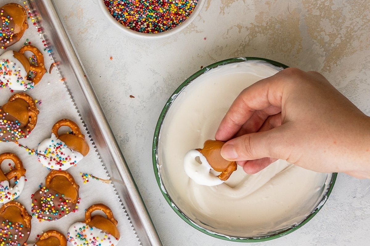 hand dipping pretzel into white chocolate 