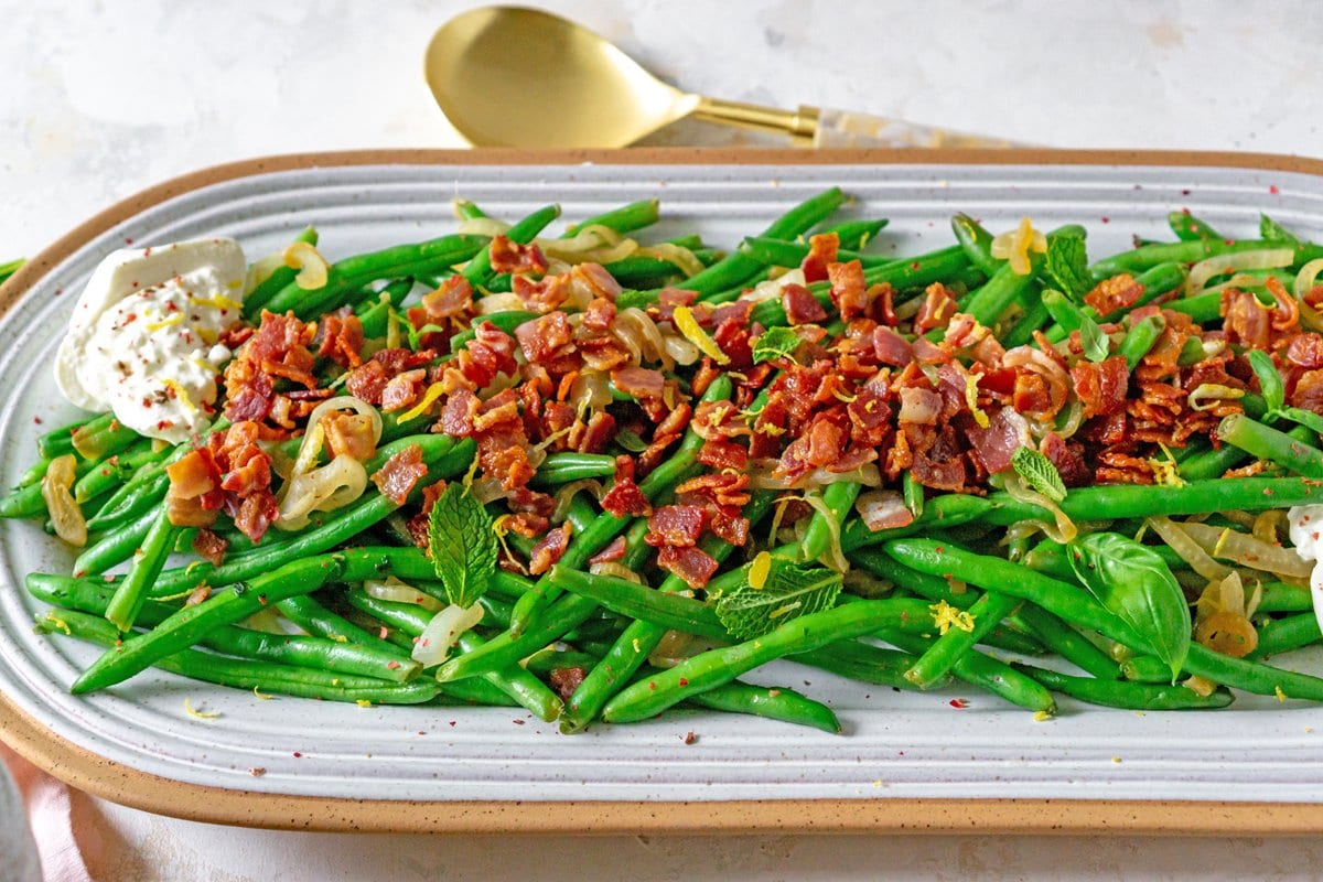 green beans with bacon on a serving dish with mint and cheese 