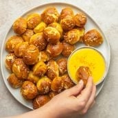 overhead of hand dipping pretzel bites into cheese sauce