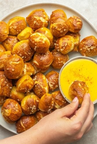 overhead of hand dipping pretzel bites into cheese sauce