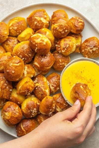 overhead of hand dipping pretzel bites into cheese sauce