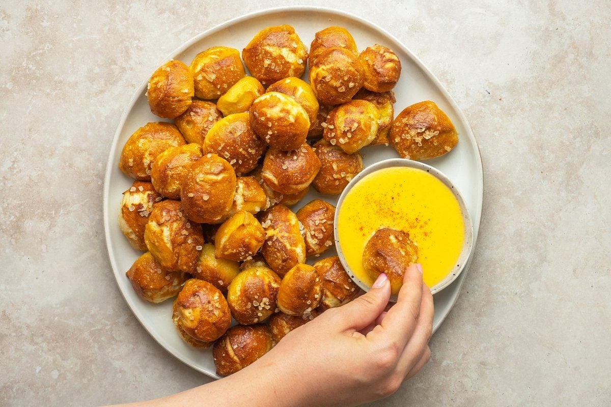 overhead of hand dipping pretzel bites into cheese sauce