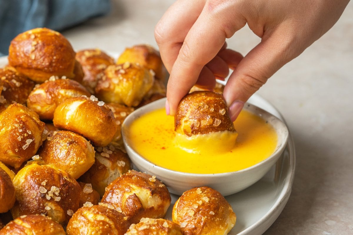 hand dipping pretzel bites into a cheese sauce 