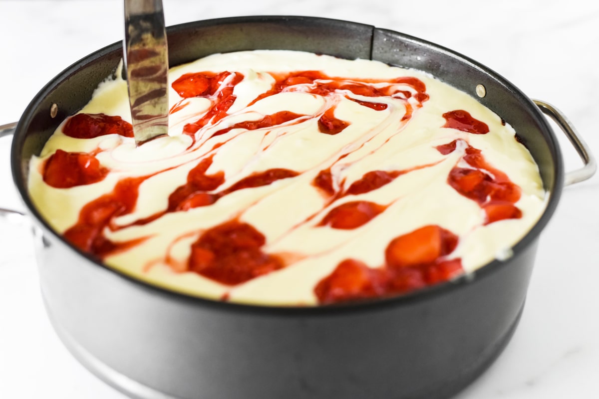 knife swirling strawberry sauce into cheesecake 