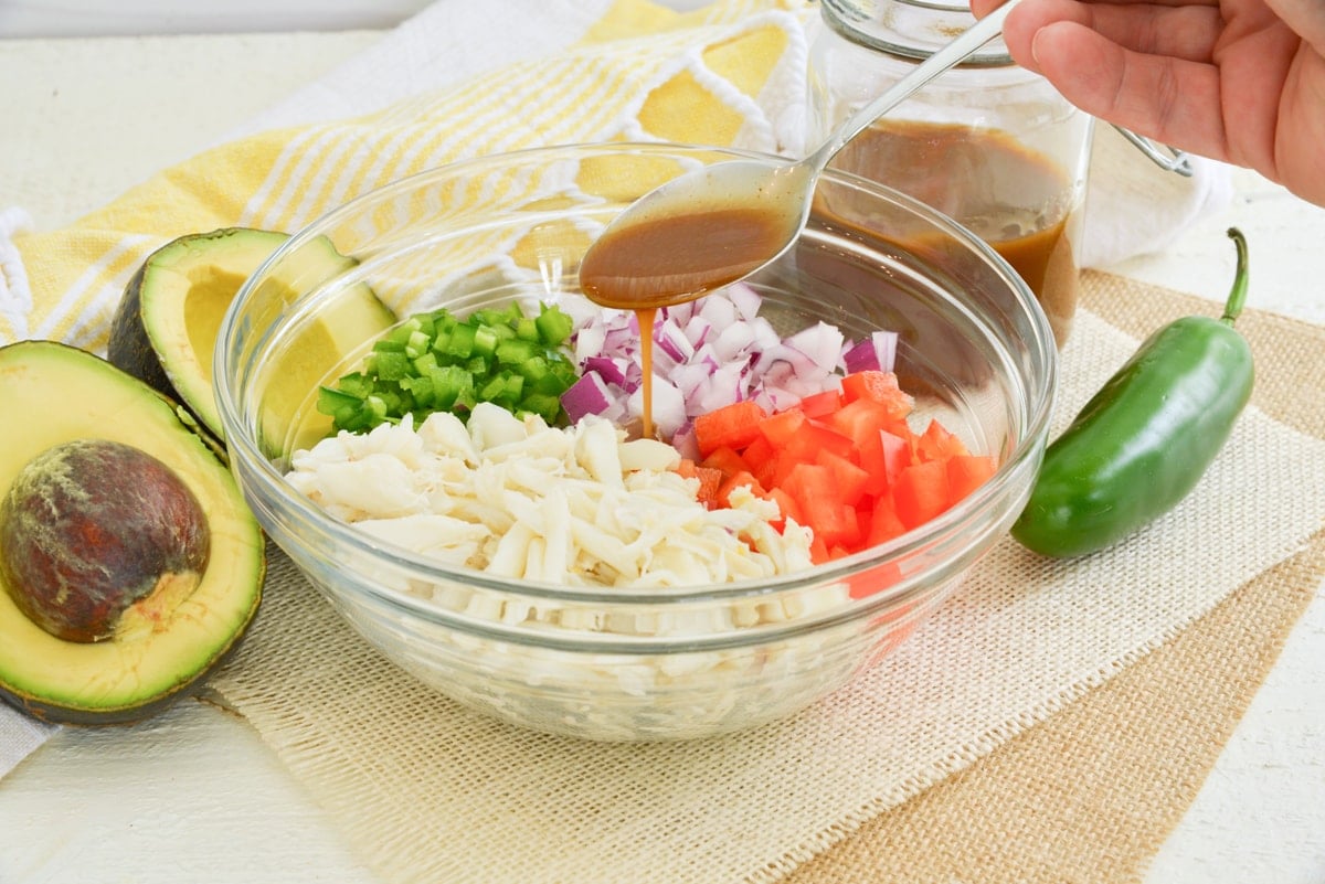 spoon drizzling dressing over crab salad ingredients 