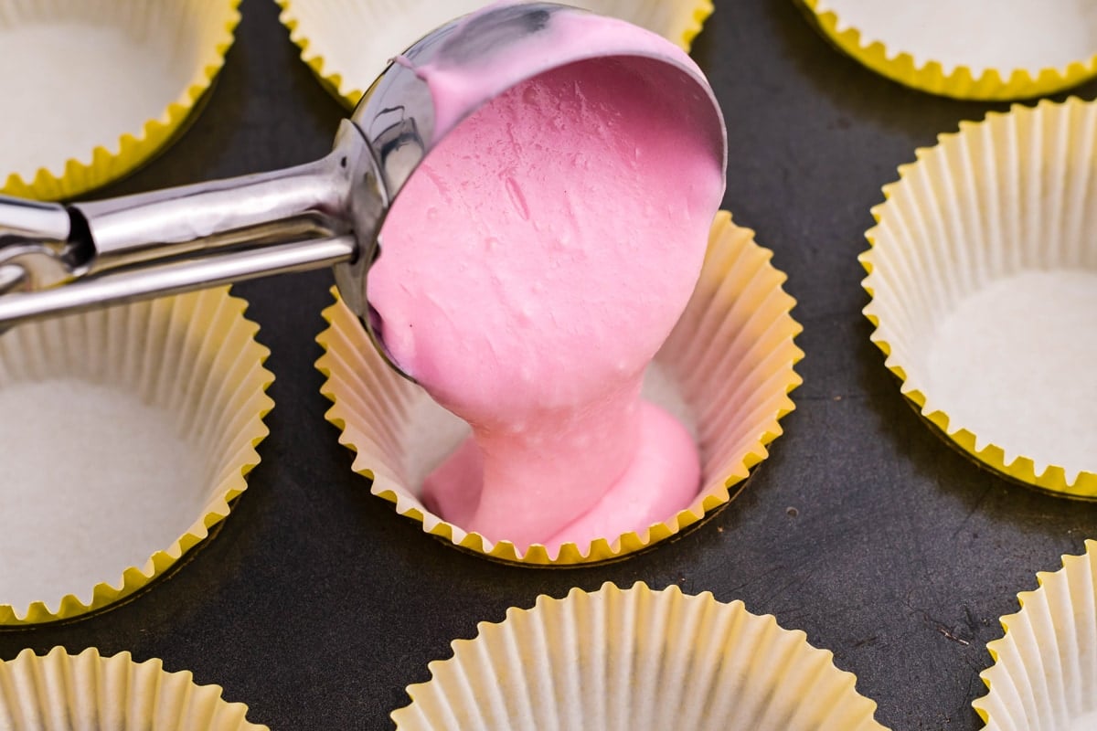 scooping pink cake batter into a muffin liner 