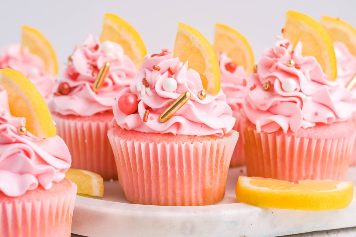 pink lemonade cupcakes lined up with lemon slices and sprinkles 