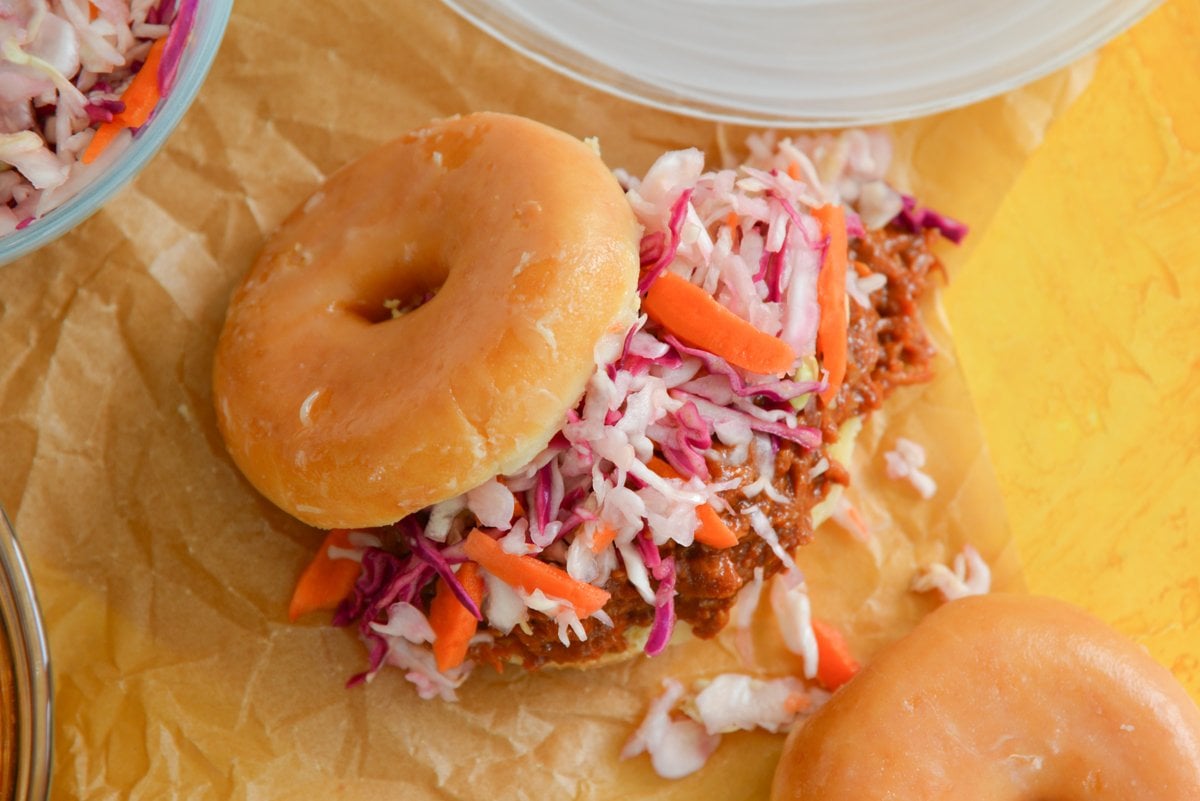 overhead of coleslaw and pulled pork falling out of a cut donut 