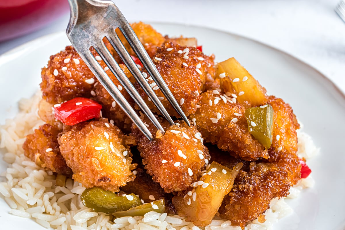 fork digging into a piece of sweet and sour chicken  