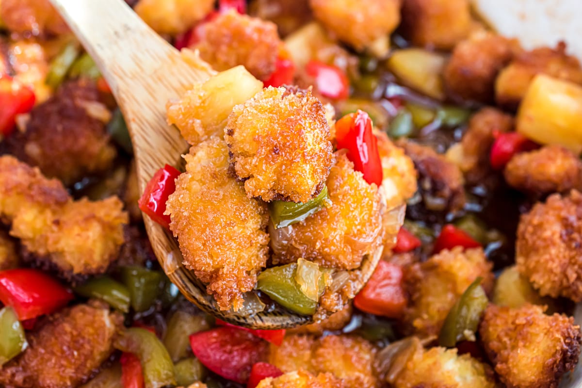 wooden spoon holding up crispy chicken in sauce 