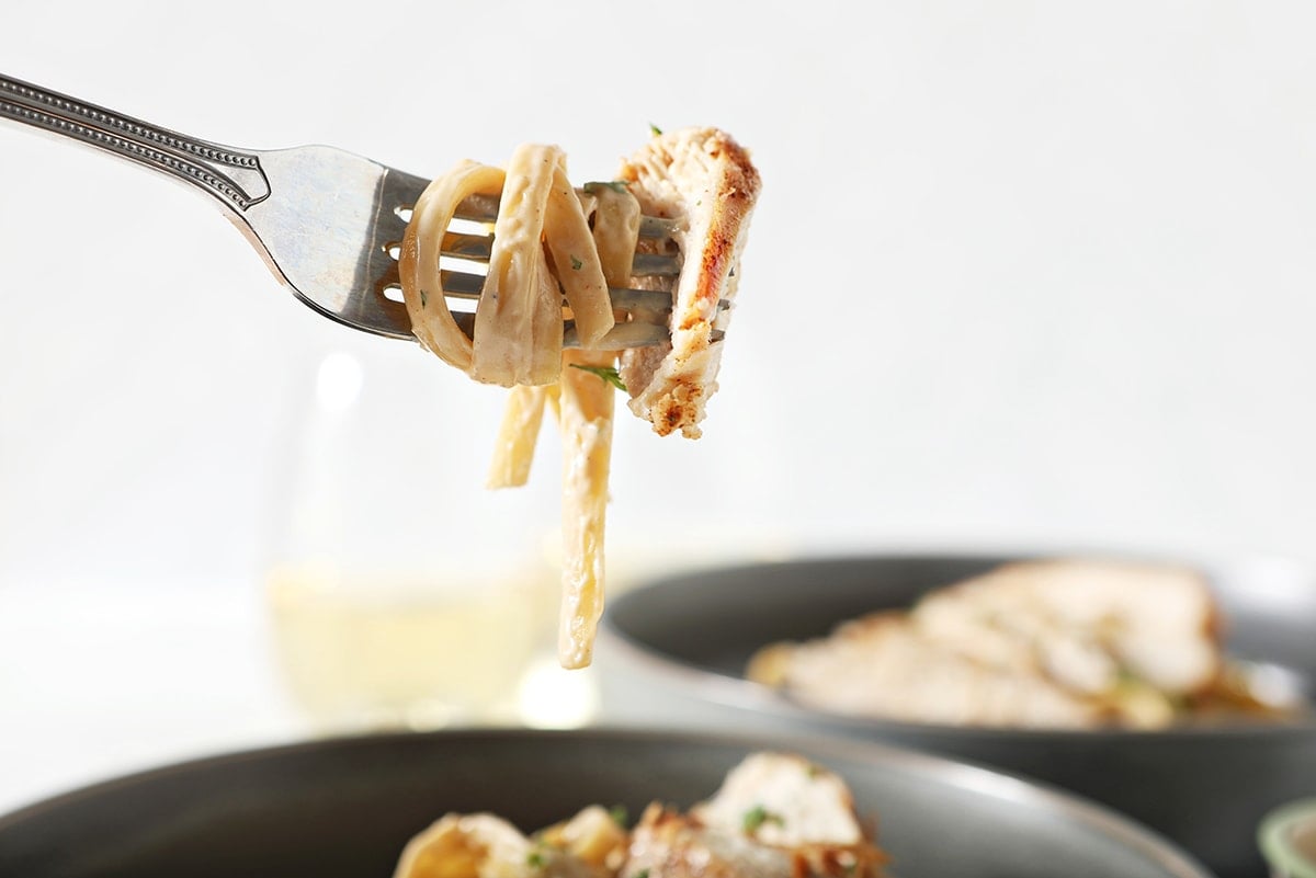 pasta swirled onto a fork with a piece of chicken 