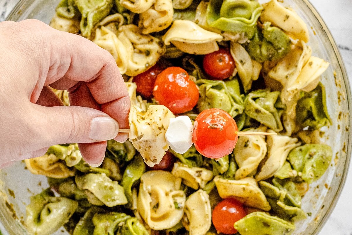 hand holding a kabob with tortellini, mozzarella cheese ball and tomato