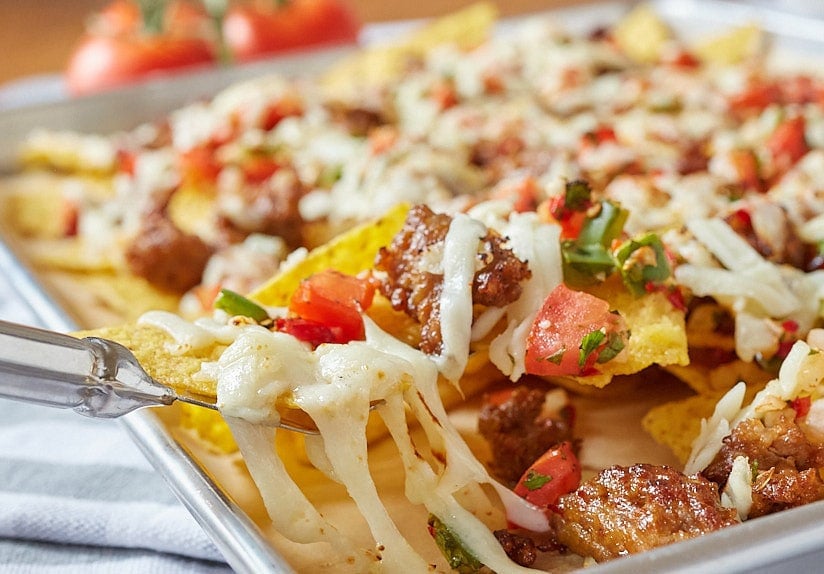 fork digging cheesy nachos off the pan 