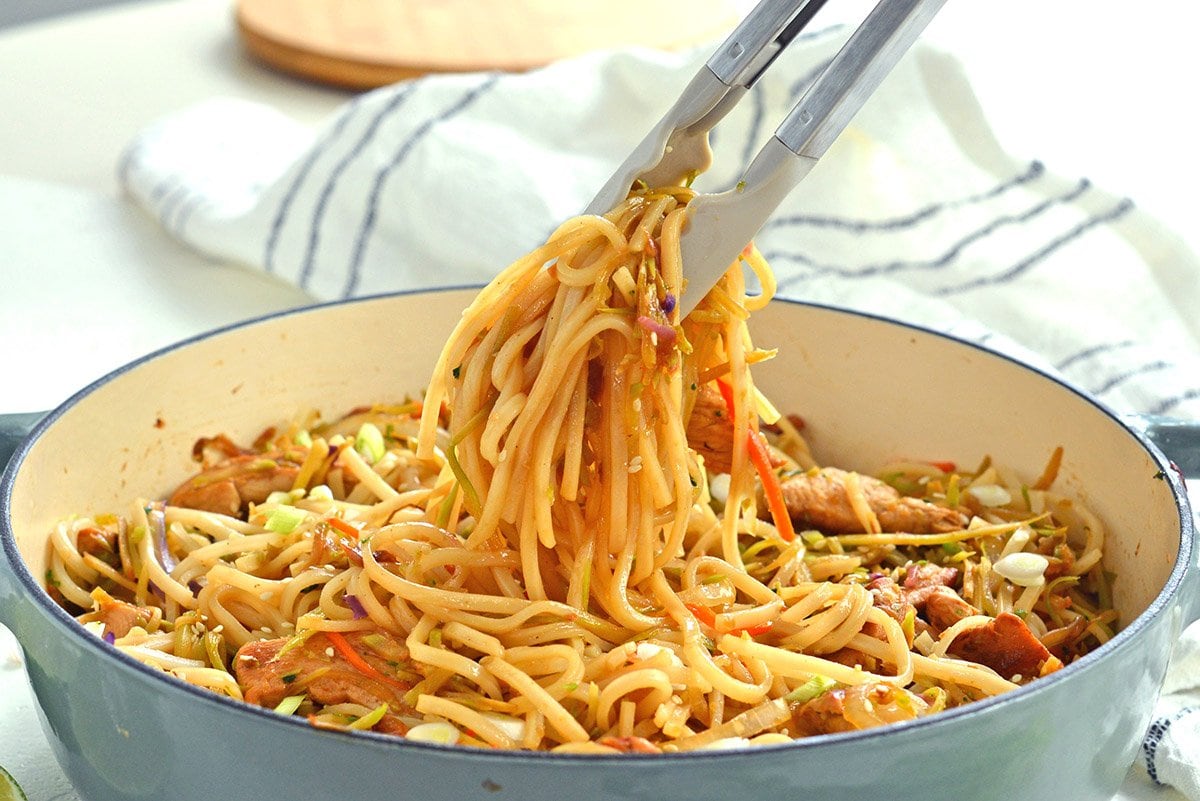 tongs picking up stir fry noodles in a pot 