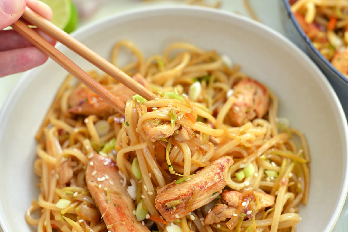 chopsticks picking up rice noodles with chicken 