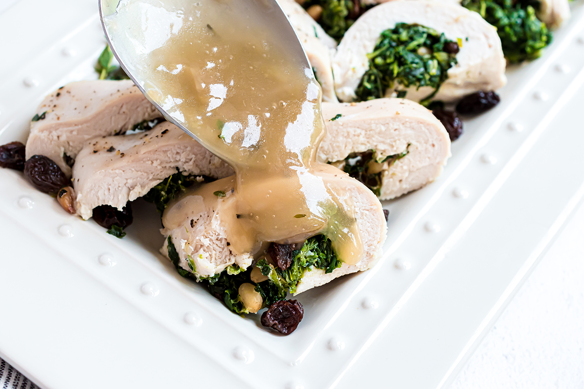 spooning gravy over spinach stuffed chicken 