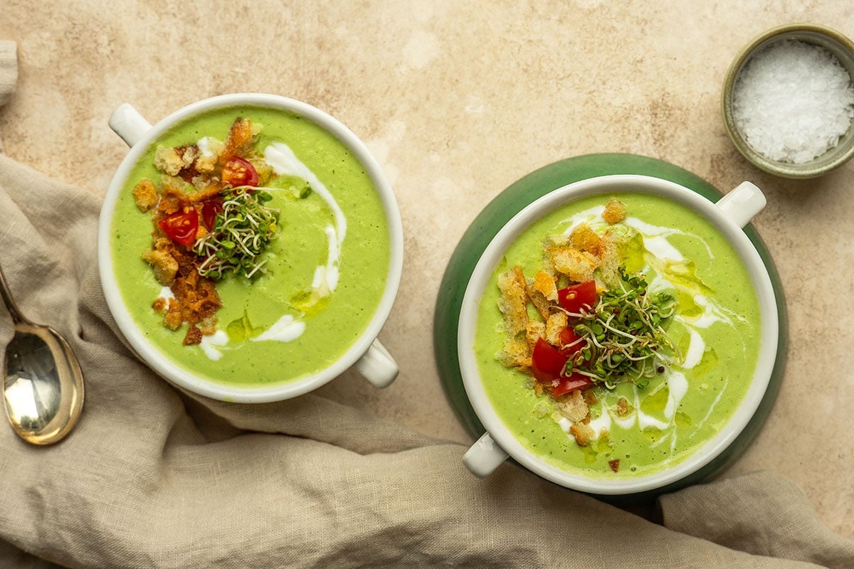 two bowls of green soup topped with tomatoes, microgreens and croutons 