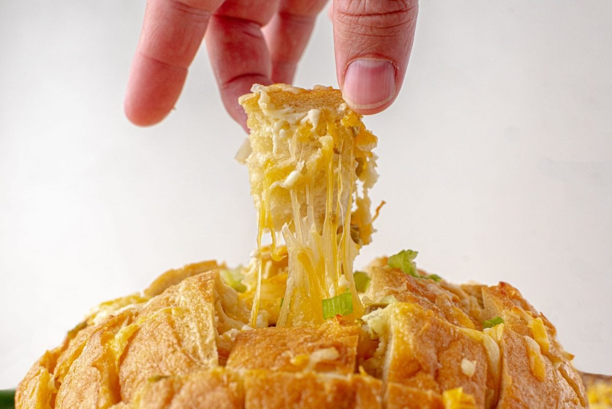 Hand pulling up a piece of cheesy bread 