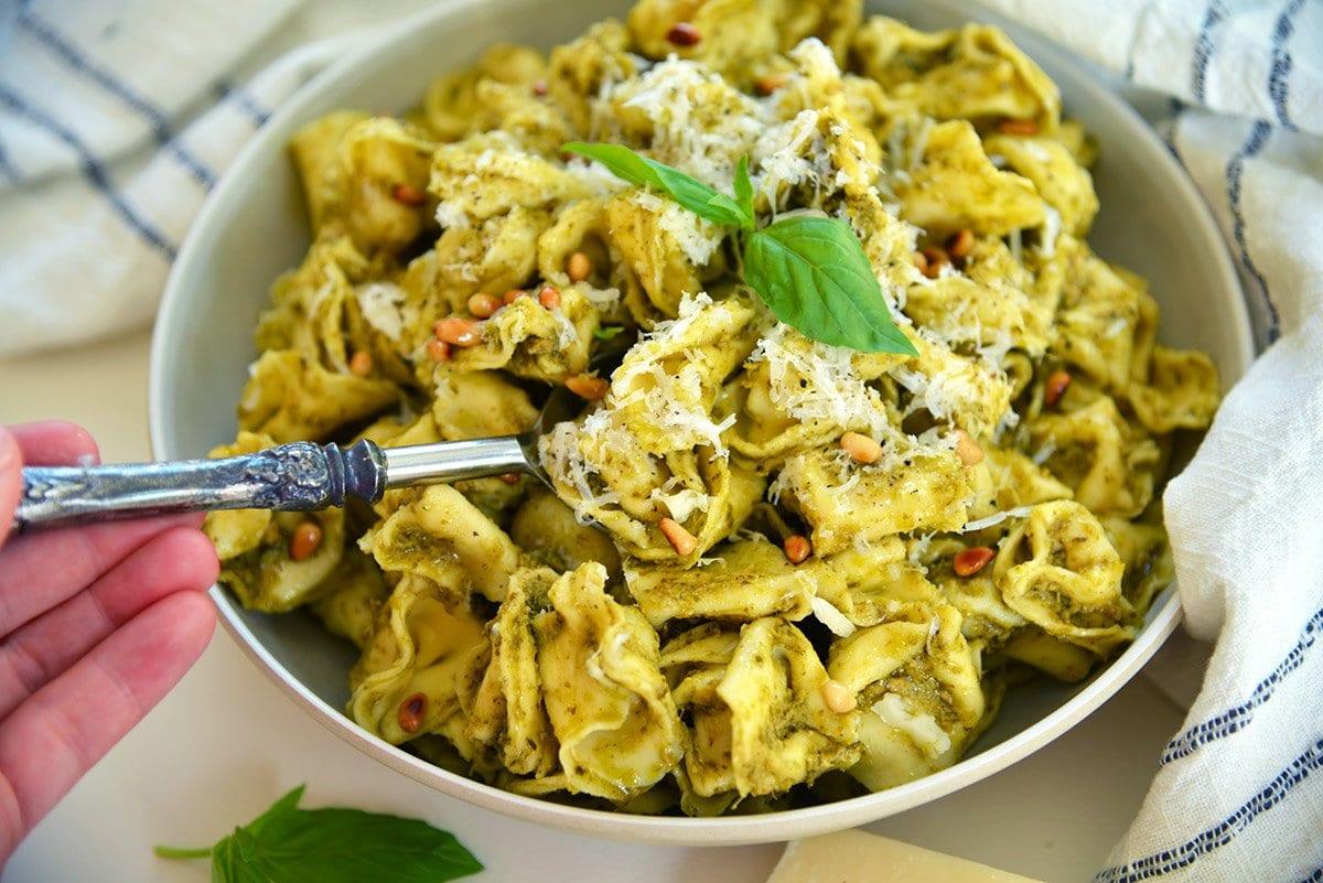 spoon digging into a bowl of tortellini in sauce