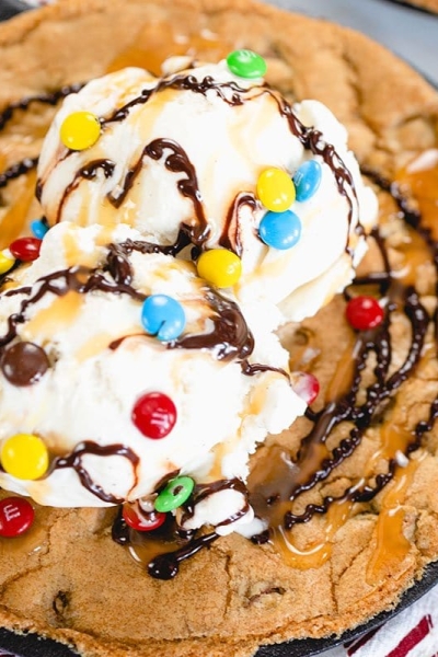 close up of skillet cookie with ice cream, sauce and m&ms