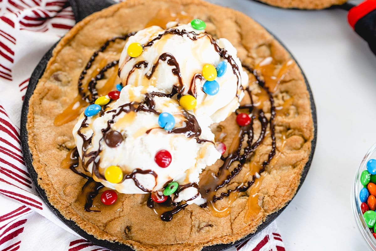 close up of skillet cookie with ice cream, sauce and m&ms