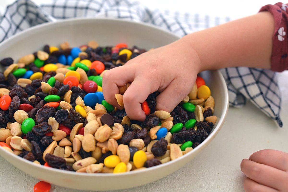 child's hand digging into a bowl of trail mix  