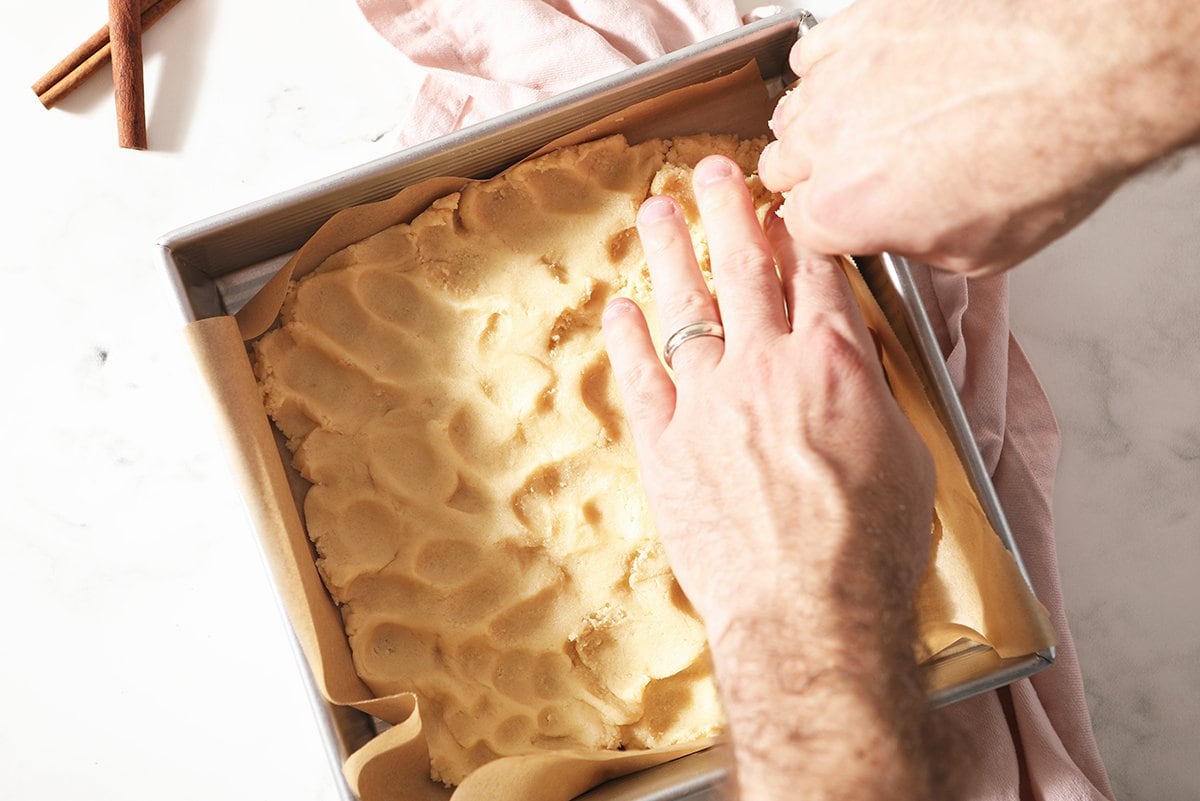 hands pressing cookie dough into a square baking pan 