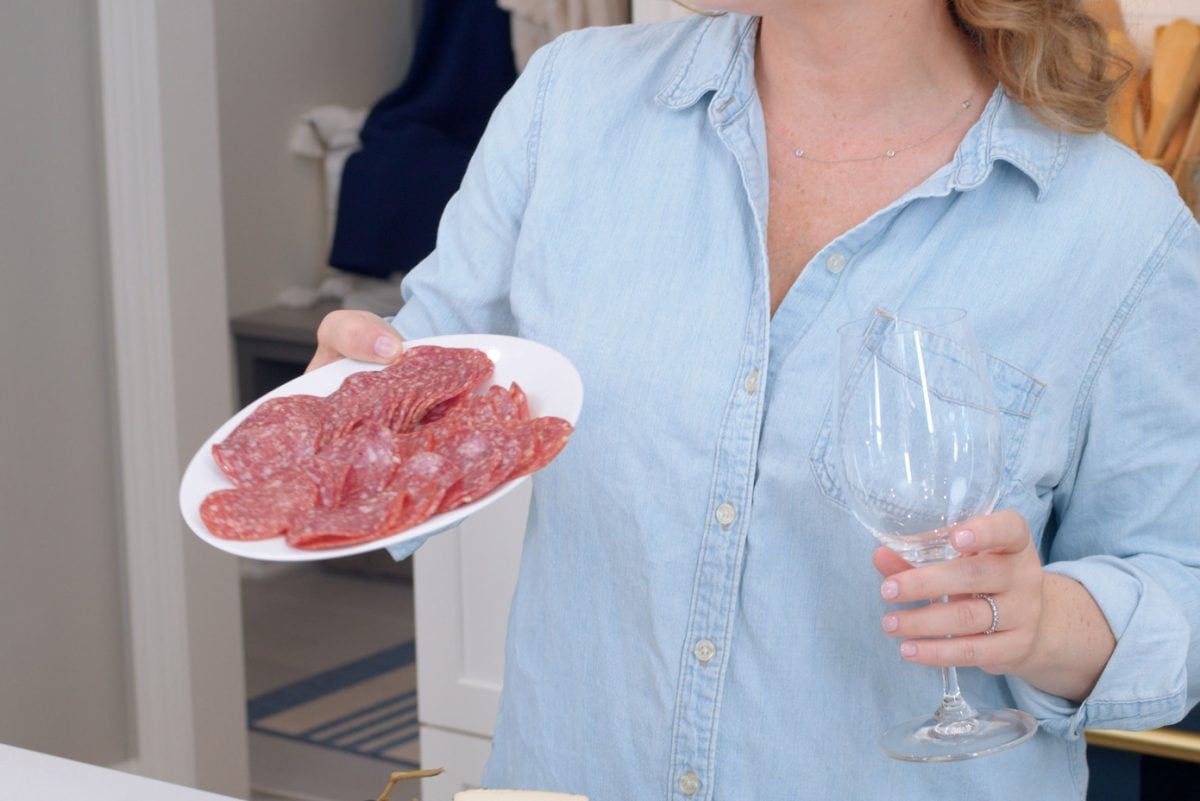 Woman holding a wine glass and a plate of sliced salami 