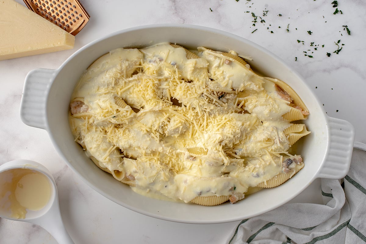sauce and cheese over stuffed shells in baking dish
