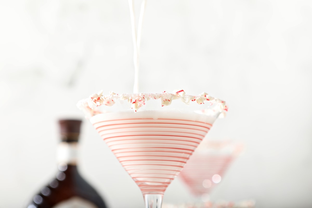 high pour of white chocolate martini into a red striped martini glass 